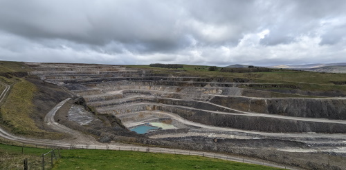 An Image showing the steps of the quarry faces. The map shows the active area where quarrying work is currently underway. Next to this, it shows the boundary where the extension is planned. Highlighted on this map, is a small woodland and hawthorne trees that will be protected from the quarry expansion. Also on the map is a point showing where some previous restoration has been carried out on the quarry.